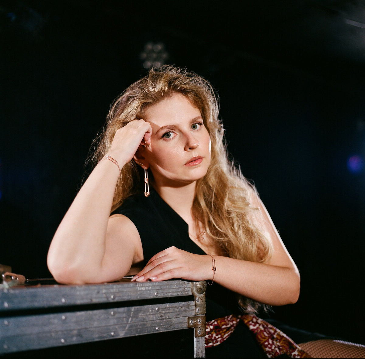 Woman leaning on a flight case, wearing 449 safety pin earrings and a bracelet