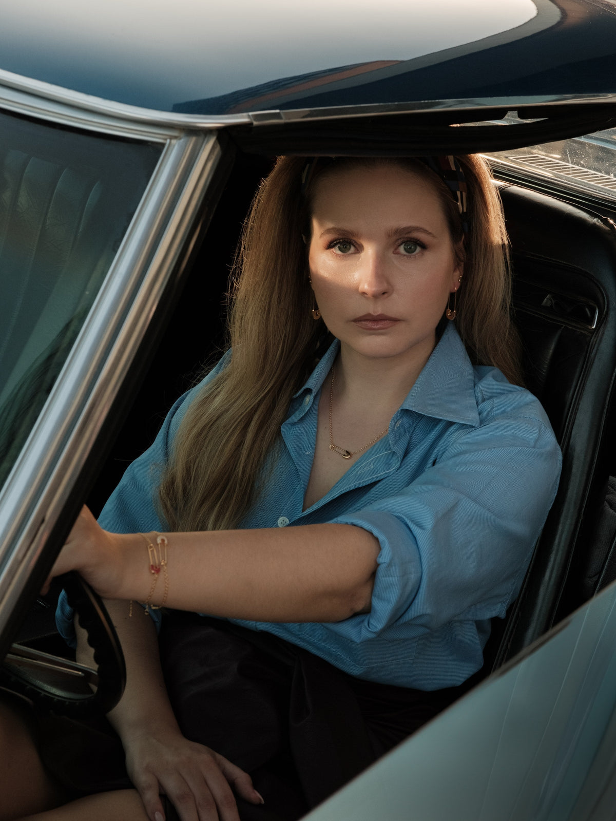 Woman in a blue shirt in a vintage car, wearing the Legacy necklace and earrings